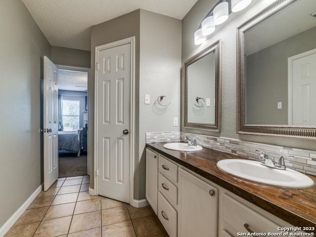 ensuite bathroom with double vanity, tile patterned flooring, decorative backsplash, and a sink