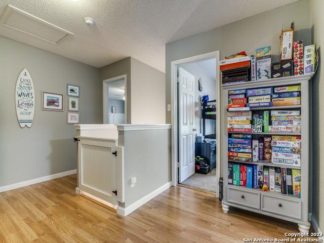 interior space featuring attic access, light wood-type flooring, a textured ceiling, and an upstairs landing