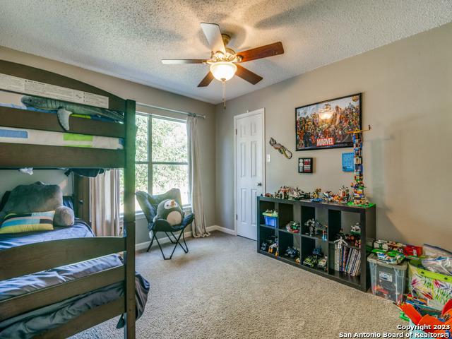 carpeted bedroom with ceiling fan, a textured ceiling, and baseboards