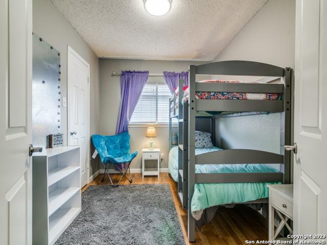 bedroom with a textured ceiling, baseboards, and wood finished floors