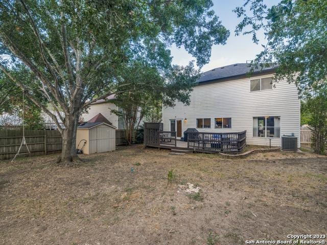 back of property with a storage shed, central AC unit, a fenced backyard, an outbuilding, and a wooden deck