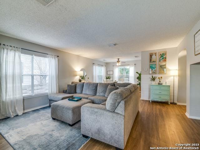 living room featuring visible vents, a textured ceiling, baseboards, and wood finished floors