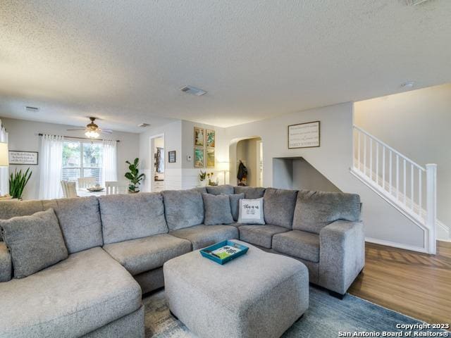 living area featuring a textured ceiling, arched walkways, wood finished floors, visible vents, and stairway