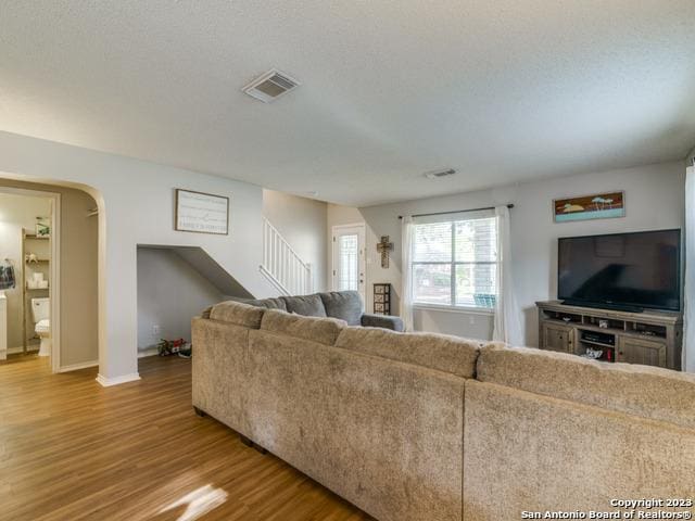 living room featuring arched walkways, wood finished floors, visible vents, baseboards, and stairs