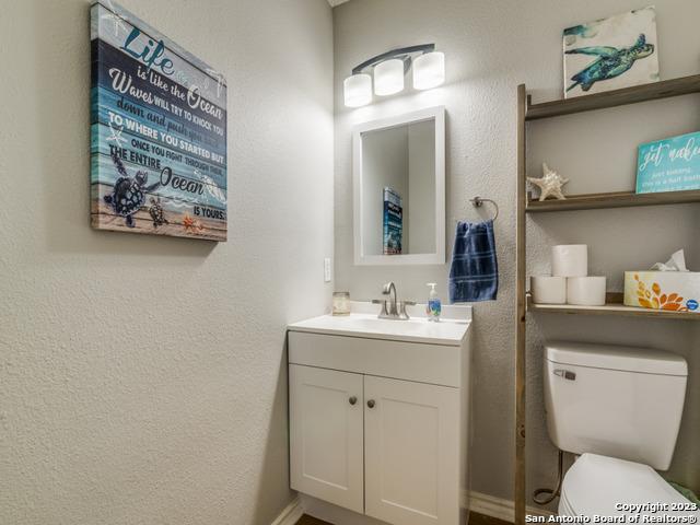 half bath with toilet, a textured wall, and vanity