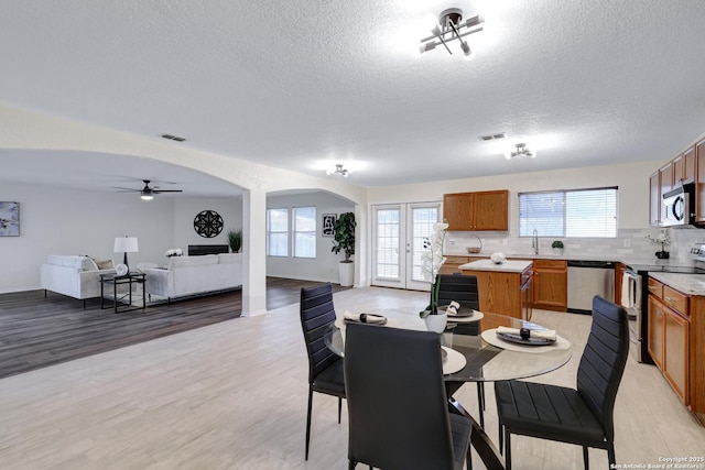 dining area with light wood-style flooring, visible vents, arched walkways, and a textured ceiling