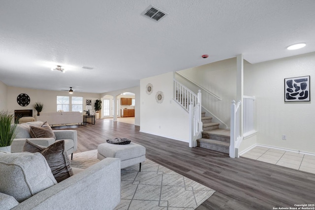 living room featuring arched walkways, visible vents, stairway, a textured ceiling, and wood finished floors