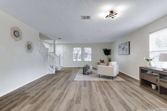 living area with visible vents, stairway, a textured ceiling, and wood finished floors