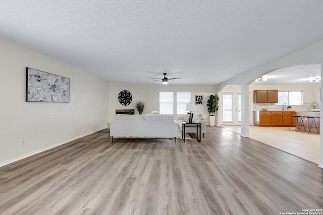 unfurnished living room with arched walkways, light wood-style floors, a sink, a textured ceiling, and baseboards