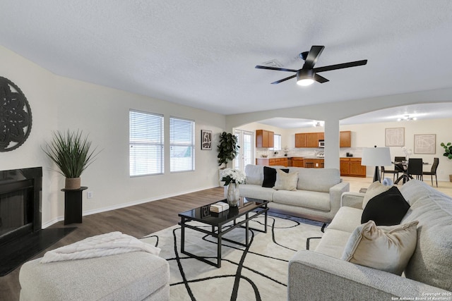 living area featuring a fireplace with flush hearth, arched walkways, light wood-style flooring, and a textured ceiling