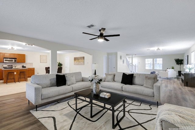 living room with arched walkways, visible vents, light wood-style flooring, and a textured ceiling