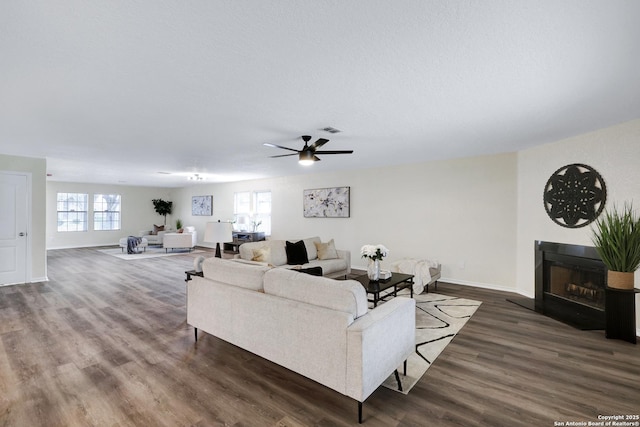 living room featuring a fireplace with raised hearth, a textured ceiling, wood finished floors, visible vents, and baseboards