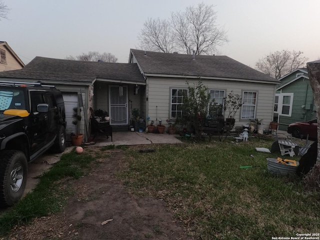 back of house featuring a garage, a shingled roof, a lawn, and a patio area