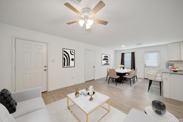 living room featuring ceiling fan, light wood finished floors, visible vents, and baseboards