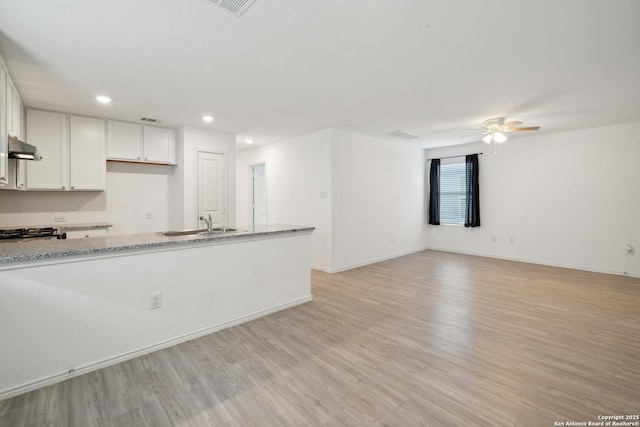 kitchen with light stone counters, under cabinet range hood, recessed lighting, white cabinetry, and light wood-style floors