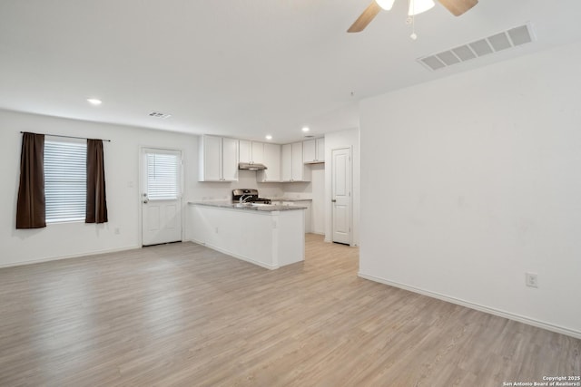 kitchen with visible vents, white cabinets, open floor plan, a peninsula, and light wood-style floors