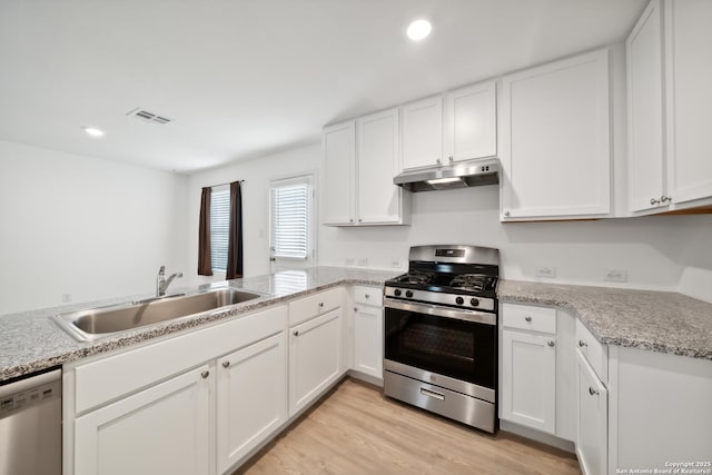 kitchen with stainless steel appliances, visible vents, light wood-style flooring, a sink, and under cabinet range hood