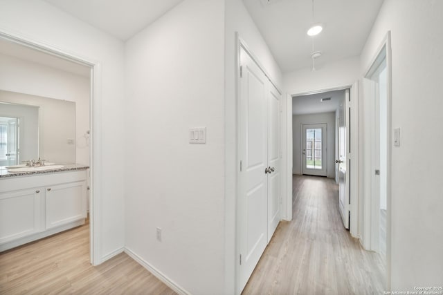 corridor featuring light wood-type flooring, a sink, attic access, and baseboards