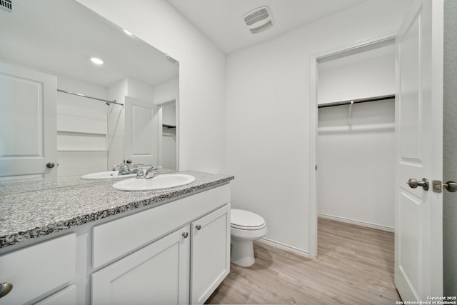 bathroom with baseboards, visible vents, toilet, wood finished floors, and a spacious closet