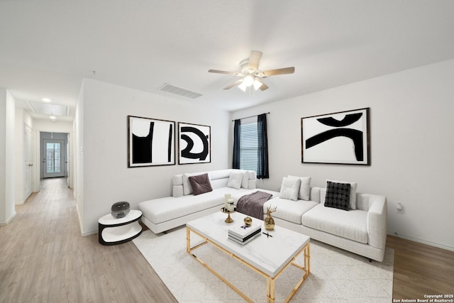 living room featuring visible vents, light wood-type flooring, attic access, and a ceiling fan