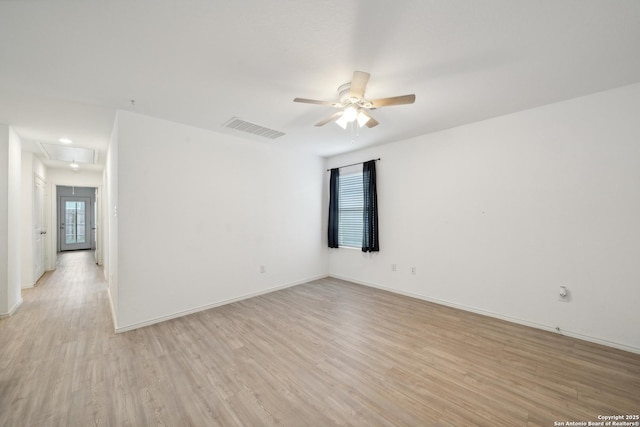 spare room featuring visible vents, light wood-style flooring, attic access, ceiling fan, and baseboards