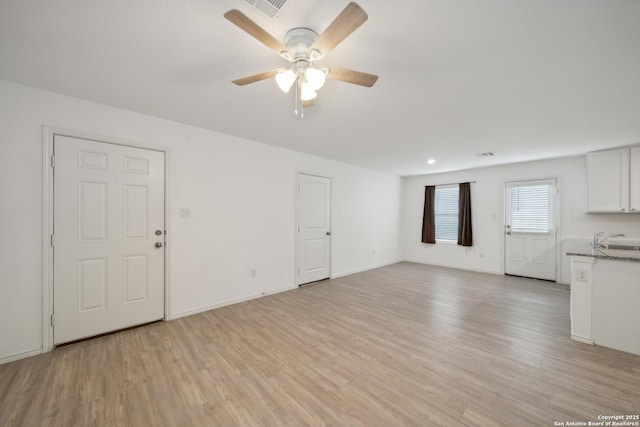 unfurnished living room featuring light wood-style floors, a sink, baseboards, and a ceiling fan