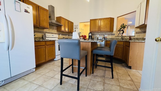 kitchen featuring white appliances, brown cabinetry, wall chimney range hood, and decorative backsplash