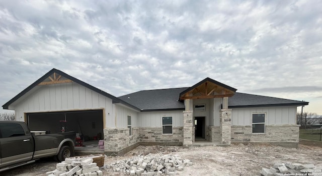 modern farmhouse featuring a garage, stone siding, a shingled roof, and board and batten siding