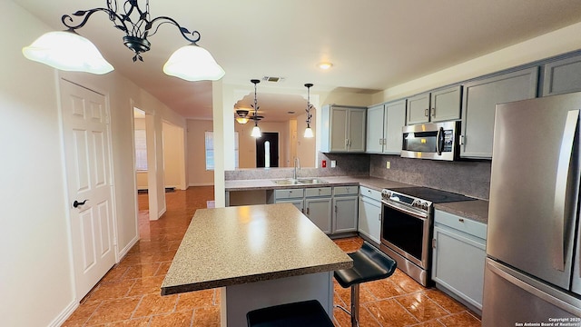 kitchen with stainless steel appliances, gray cabinets, a sink, a kitchen island, and a kitchen bar