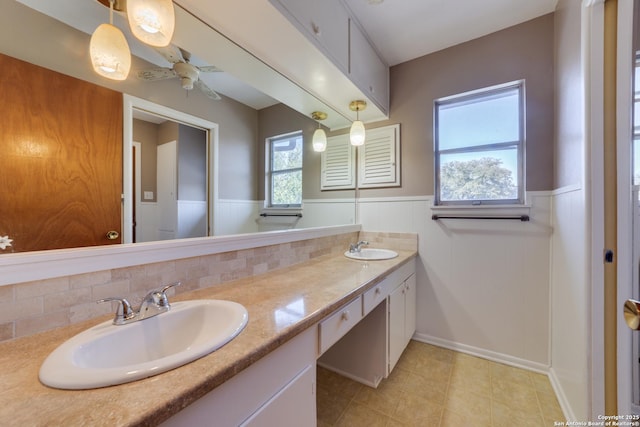 full bathroom featuring double vanity, a ceiling fan, a sink, and wainscoting