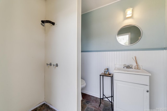 bathroom with stone finish flooring, wainscoting, vanity, and toilet