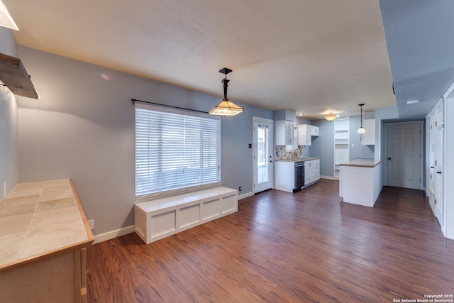 kitchen featuring dark wood-type flooring, white cabinets, hanging light fixtures, and baseboards