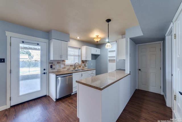 kitchen featuring a peninsula, a sink, white cabinetry, stainless steel dishwasher, and dark wood-style floors