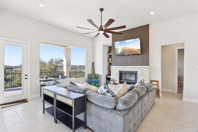 living area featuring recessed lighting, ceiling fan, a stone fireplace, and baseboards