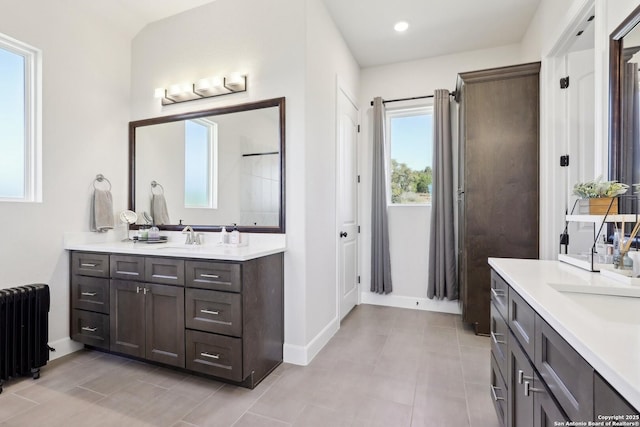 full bathroom featuring baseboards, two vanities, a sink, and radiator heating unit