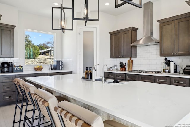 kitchen featuring light countertops, stainless steel gas cooktop, wall chimney range hood, and dark brown cabinets