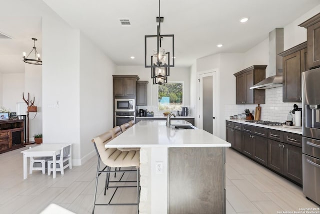 kitchen with a chandelier, a sink, light countertops, appliances with stainless steel finishes, and wall chimney exhaust hood