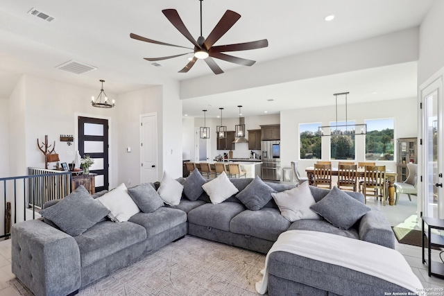 living area featuring ceiling fan with notable chandelier, recessed lighting, visible vents, and light tile patterned floors