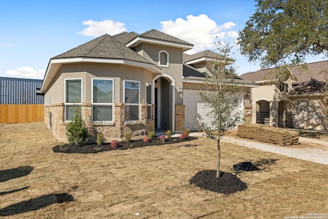 view of front of house with stucco siding, concrete driveway, an attached garage, fence, and stone siding