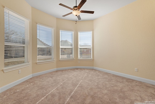 carpeted spare room featuring baseboards and a ceiling fan