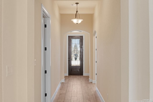 entryway featuring arched walkways, light wood-style flooring, and baseboards