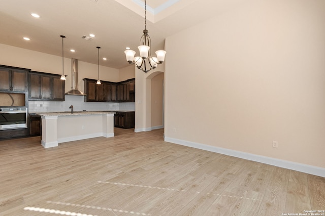 kitchen featuring arched walkways, oven, light countertops, decorative backsplash, and wall chimney exhaust hood