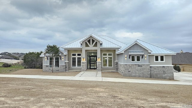 view of front of house with stone siding, french doors, metal roof, and a standing seam roof