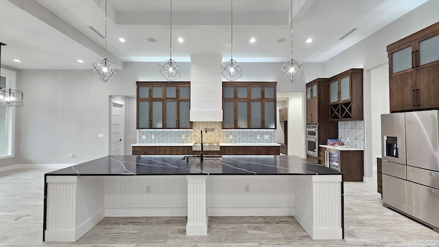 kitchen featuring dark brown cabinetry, decorative backsplash, a large island, glass insert cabinets, and a sink