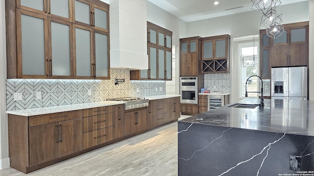 kitchen with backsplash, appliances with stainless steel finishes, light wood-style floors, glass insert cabinets, and a sink