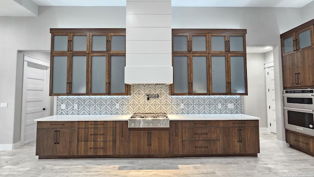 kitchen featuring glass insert cabinets, light countertops, backsplash, and appliances with stainless steel finishes