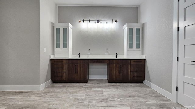 bathroom with a textured wall, double vanity, a sink, and baseboards