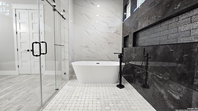 bathroom featuring a freestanding tub, a marble finish shower, and tile walls