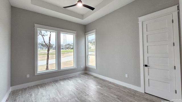 unfurnished room with ceiling fan, wood finished floors, a raised ceiling, and baseboards