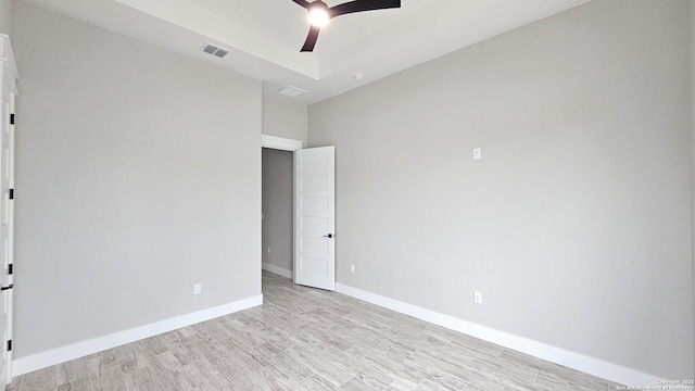 unfurnished bedroom featuring visible vents, baseboards, a raised ceiling, ceiling fan, and light wood-type flooring